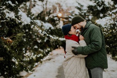 Neşeli bir çift, ışıl ışıl ışıkların ve sakin bir parkta yumuşak karın ortasında samimi bir kucaklaşmanın tadını çıkarır. Yürek ısıtan bir kış sahnesi yakalar..