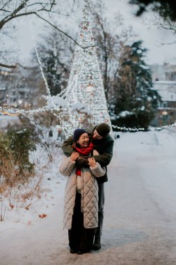 Karlı bir parkta, Koreli bir kadın ve beyaz bir erkek birbirlerine gülümseyip sarılıyorlar. Ağaçlar ışıklarla süslenip kış atmosferine ekleniyor..