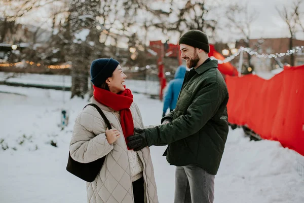 Koreli bir kadın ve beyaz bir erkek karlı bir parkta gülüşüyor ve gülüyorlar. Birbirlerine yakın dururlar, sıcak giysilere bürünürler, kış atmosferinin tadını çıkarırlar..