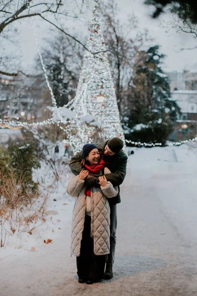 Karlı bir parkta, Koreli bir kadın ve beyaz bir erkek birbirlerine gülümseyip sarılıyorlar. Ağaçlar ışıklarla süslenip kış atmosferine ekleniyor..