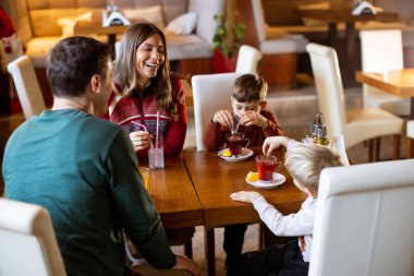 Bir aile bir restoranda ahşap bir masanın etrafında oturur. Birbirleriyle konuşup gülerken içkileri ve abur cuburları paylaşıyorlar. İki çocuk masada anne babalarıyla takılıyor..