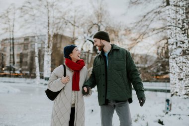 Koreli bir kadın ve beyaz bir adam karlı bir parkta birlikte yürüyorlar. Birbirlerine bakarken gülümsüyor ve el ele tutuşuyorlar. Ağaçlar ışıklarla süslenmiş..