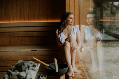 Bir kadın, ahşap bir saunada huzurlu bir anın tadını çıkarırken dinlendirici bir sıcaklıkla gününün tadını çıkarır..