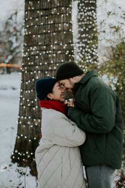 Koreli bir kadın ve beyaz bir adam parka yakın duruyorlar. Kışın, karlı bir manzara ve ağaçlardaki tatil ışıklarıyla çevrili sıcak bir anı paylaşıyorlar..