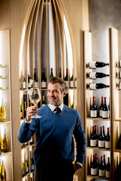 Kendine güvenen bir şarap garsonu şık bir şarap mahzeninde bir anlık takdirin tadını çıkarır. Raflarda güzel bir zemin oluşturan kaliteli şarap şişeleri var..