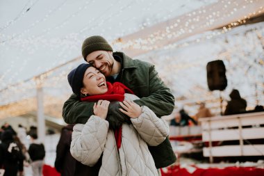 Koreli bir kadın ve beyaz bir erkek kış festivalinde neşeli bir anı paylaşıyorlar. Parlak ışıklar ve şenlikli dekorasyonlarla çevrili, canlı bir atmosfer yaratıyorlar..