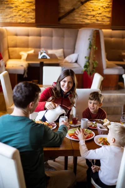 Bir aile kahvaltı sırasında bir restoranda bir masanın etrafında oturur. Çocuklar yemek yiyip sohbet ederken anne içki servisi yapar. Hava sıcak ve davetkar..