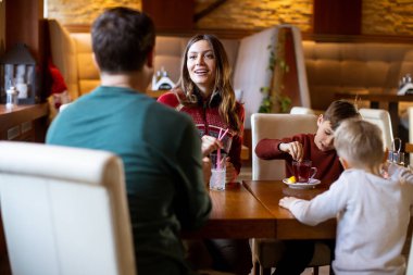 Bir aile restoran masasında toplanır. Çocuklar içkileriyle ve atıştırmalıklarıyla oynarken yetişkinler konuşuyor ve gülümsüyor. Ortam sıcak ve yumuşak ışıklandırmayla davetkar..