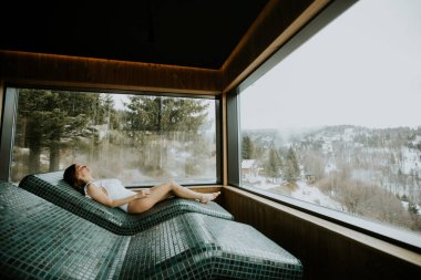 Sıcak taş bir yatakta uzanan bir kadın, dışarıdaki sisli dağlara bakarken lüks bir kaplıcada sükuneti kucaklıyor..