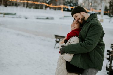 Koreli bir kadın ve beyaz bir adam karlı bir parkta bir anı paylaşıyorlar. Bir kış günü, arka planda banklar ve tatil ışıklarıyla çevrelenmiş, birbirlerine gülümsüyorlar..