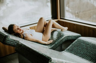 Kaplıcadaki sıcak taş bir yatakta yatan bir kadın. O, sıcak yüzeyi ve dışarıdaki manzarayı sever. Sıcacık ve davetkar bir ortam. Soğuk bir günde rahatlamak için mükemmel..