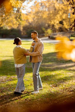 Koreli bir kadın ve beyaz bir erkek, canlı bir parkta, sıcak sonbahar güneşi altında neşeli bir dans ediyorlar. Kahkaha havayı dolduruyor..