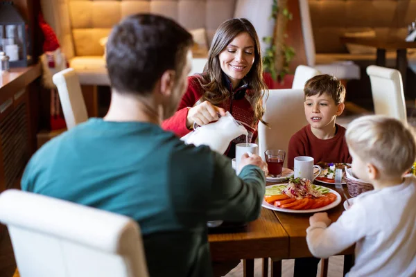 Bir aile restoranda bir masada oturur. Çocuklar kahvaltı yaparken, ebeveyn bardağa süt döker. Tabaklarda çeşitli yiyecekler ve içecekler var..