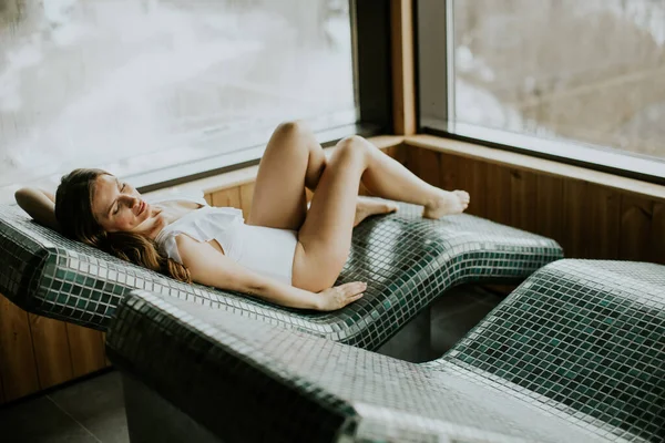 Kaplıcadaki sıcak taş bir yatakta yatan bir kadın. O, sıcak yüzeyi ve dışarıdaki manzarayı sever. Sıcacık ve davetkar bir ortam. Soğuk bir günde rahatlamak için mükemmel..