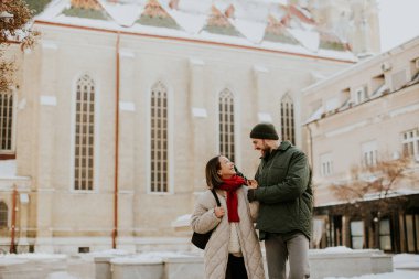 Koreli bir kadın ve Kafkasyalı bir adam Timisoara 'daki Aziz George Katedrali yakınlarında karda yürüyorlar. İkisi de gülümsüyor ve birbirlerine bakıyorlar..