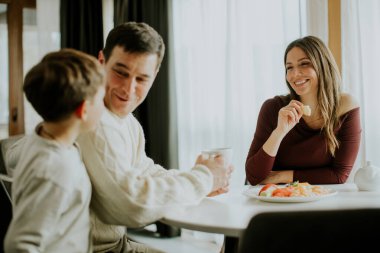 Bir adam ve bir kadın bir çocukla aynı masada oturuyorlar. Kahkahaları ve yiyecekleri paylaşıyorlar, bardaktan içiyorlar. Parlak ışık pencerelerden içeri girer ve yemek için sıcak bir atmosfer yaratır..