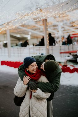 Koreli bir kadın durup gülümserken beyaz bir adam ona arkadan sarılıyor. Açık havada, kışın ışıklarla süslenmiş bir yerdeler. Kar yere düştü..