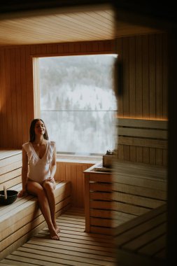 Bir kadın ahşap bir saunada dinleniyor. Bir bankta oturuyor ve dışarıdaki karın tadını çıkarıyor. Sahne, doğal ışığın içeri aktığı rahat bir atmosferi gösteriyor..