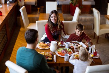 Bir aile bir restorandaki bir masada kahvaltıyı paylaşır. Sahnede çeşitli yemekleri, içkileri ve kahkahaları olan iki yetişkin ve iki çocuk görülüyor. Rahatlatıcı bir sabah toplantısı..