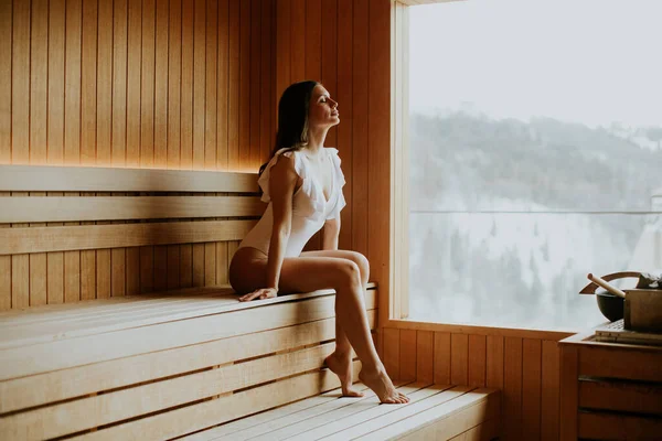 Bir kadın saunada ahşap bir bankta oturuyor. Pencereden karla kaplı manzaraya doğru bakıyor. Etrafındaki sıcak havada buhar yükseliyor..