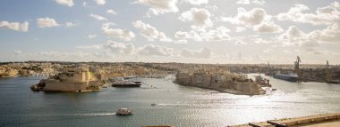 Grand Harbour 'un geniş bir manzarası, sudaki tarihi binaları ve tekneleri gösteriyor. Bulutlar, Malta Valletta 'daki hareketli limana ve çevreleyen manzaraya zemin hazırlar..
