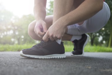 Koşan adam ayakkabı bağcıklarını bağlıyor.