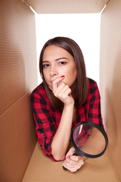 Feminino espreitando na caixa de papelão olhando através de lupa — Fotografia de Stock