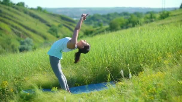 Νεαρή γυναίκα κάνει γιόγκα στο πράσινο λιβάδι του καλοκαιριού — Αρχείο Βίντεο