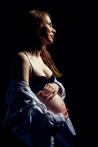Perfil da mulher grávida sobre fundo preto sentindo calma com os olhos fechados — Fotografia de Stock