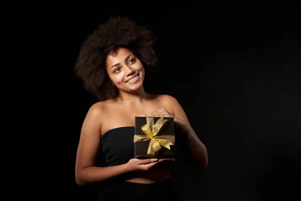 黒金曜日の販売 贈り物 プレゼント お祝いのコンセプト 幸せなアフロ系アメリカ人女性を保持しています1つの黒のギフトボックス上に金色の弓黒の背景 空のコピースペースを見て — ストック写真