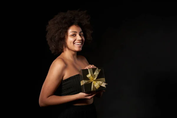 黒金曜日の販売 贈り物 プレゼント お祝いのコンセプト 幸せなアフロ系アメリカ人女性を保持している1つの黒のギフトボックスで黒の背景の上に黄金の弓 カメラを見て — ストック写真