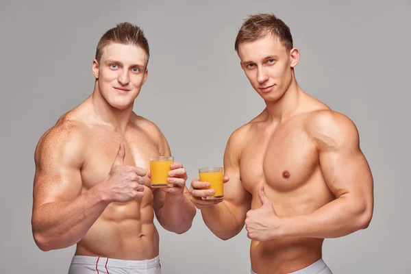 Dois homens atléticos com copos de suco de laranja — Fotografia de Stock