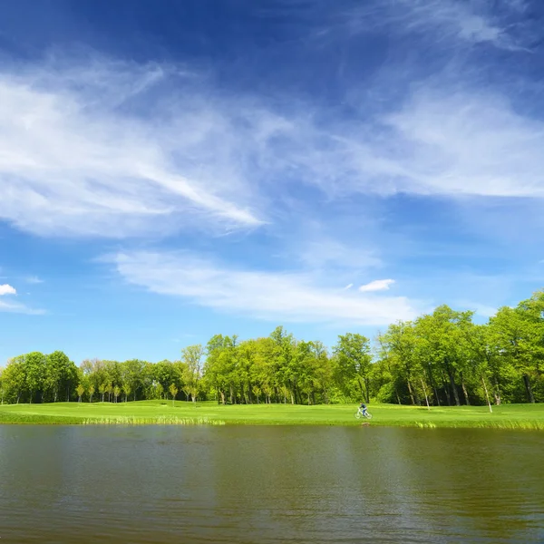 Joki ja vihreä nurmikko, mies pyörällä — kuvapankkivalokuva
