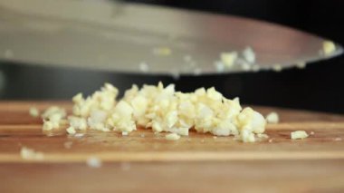 Taze sarımsak karanfilleri, keskin bir bıçakla yontulup, kırsal bir ahşap kesme tahtasıyla doğranarak, temel yemek hazırlama tekniğini gösteriyor.