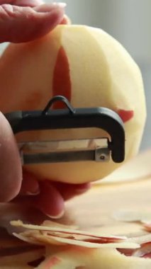 Tahta kesme tahtasındaki büyük kırmızı elmayı soymaya yakın.