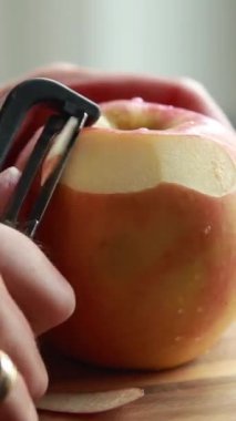 Tahta kesme tahtasındaki büyük kırmızı elmayı soymaya yakın.