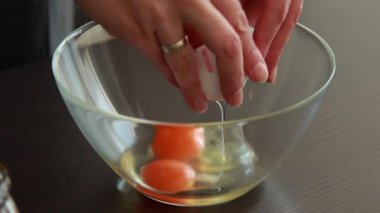 Kadın elleri cam kasede yumurta kırıyor.