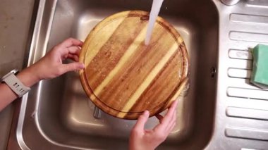Kız mutfak lavabosunda ahşap kesme tahtasını yıkıyor.