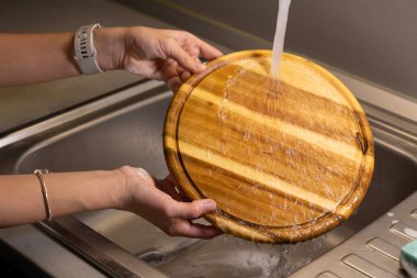 Kız mutfak lavabosunda tahta kesme tahtası yıkıyor.