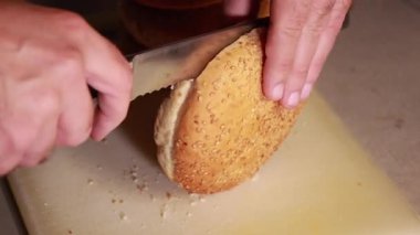 Adam mutfakta tahta kesme tahtasıyla ekmeği ikiye bölüyor.