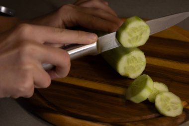 Mutfakta tahta kesme tahtasının üzerinde taze salatalık dilimliyorum.