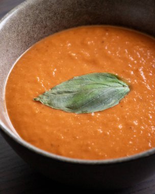 Kızarmış domates ve siyah kasede fesleğenli kırmızı çan biberi çorbası.