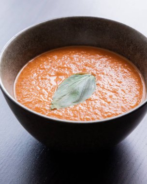 Kızarmış domates ve siyah kasede fesleğenli kırmızı çan biberi çorbası.