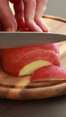 Çiğ kırmızı bir elmanın ahşap bir kesme tahtasıyla yarım ay şeklinde dilimlendiği yakın plan.