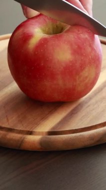 Çiğ kırmızı bir elmanın ahşap bir kesme tahtasıyla yarım ay şeklinde dilimlendiği yakın plan.