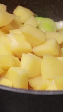 Yakın plan doğranmış pırasa ve patates parçaları tencerede birlikte pişiyor.