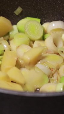 Yakın plan doğranmış pırasa ve patates parçaları tencerede birlikte pişiyor.