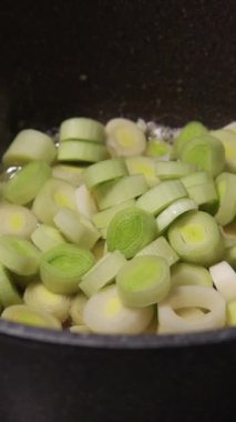 Yakın plan doğranmış pırasa ve patates parçaları tencerede birlikte pişiyor.