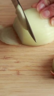 Kadınların elleri, soyulmuş sarı soğanı ahşap bir kesme tahtasının üzerinde yarım daire şeklinde dilimliyor.