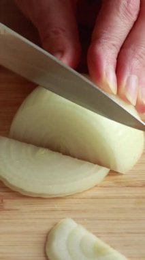 Kadınların elleri, soyulmuş sarı soğanı ahşap bir kesme tahtasının üzerinde yarım daire şeklinde dilimliyor.